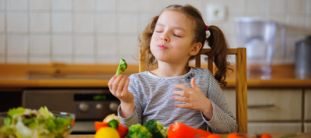 Una niña pequeña come brócoli y le gusta mucho.